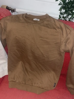 Brun sweatshirt från yourturn  - Säljer en enkel brun sweatshirt från yourturn med rund hals och ribbade muddar vid ärmslut och nederkant. Tröjan är gjord i mjukt bomullsmaterial och har en klassisk passform som är perfekt för en avslappnad look.