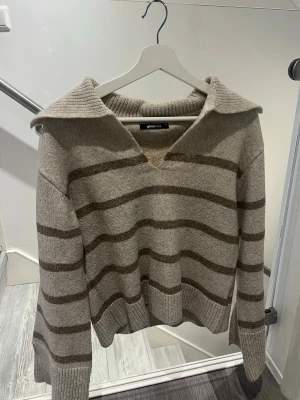 Beige stickad tröja från Ginatricot, XS - Beige stickad tröja från Ginatricot med bruna ränder. V-ringad med långa ärmar och slits vid ärmarna. Tröjan är sparsamt använd. Säljer då det inte är min stil längre. Pris kan diskuteras💖