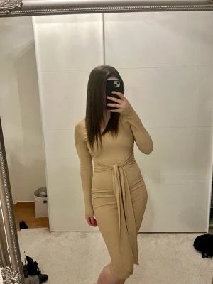 Beige ribbad omlottklänning - Trendig beige ribbad klänning med lång ärm och v-ringning. Klänningen har omlottdetalj med knytband i midjan som ger en snygg siluett. Perfekt för dig som gillar stilrena och bekväma plagg.