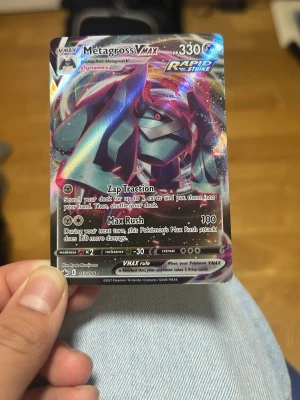 Pokémonkort Metagross VMAX - Säljer ett Metagross VMAX Pokémonkort med holografisk yta och färgstark design. Kortet har 330 HP och tillhör Rapid Strike-serien. Perfekt för samlare eller dig som vill förstärka din lek med en kraftfull VMAX.