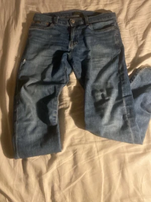 Blå jeans från Polo Ralph Lauren - Säljer ett par klassiska blå jeans från Polo Ralph Lauren. Jeansen har rak passform, fem fickor och snygga kontrastsömmar. Tillverkade i slitstark denim med knappgylf och diskret logga på knappen. Perfekta till en avslappnad och trendig stil.