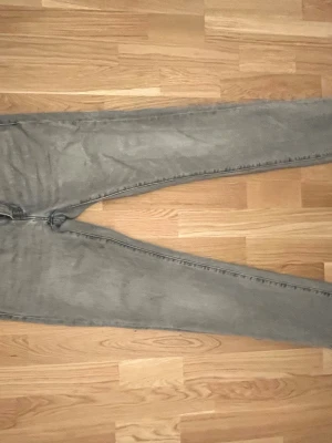 Gråa raka jeans från Levi's - Säljer ett par gråa jeans från Levi's med klassisk rak passform och femficksdesign. Jeansen har diskreta slitningar och Levi's ikoniska bakfickor med söm. Perfekta till en avslappnad stil och tillverkade i bomullsdenim. Priset går att diskuteras 