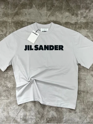 Jil Sander T-shirt  - Jil Sander t-shirt. Helt ny med tags kvar. Tillverkad i mjuk bomull med en premium känsla och ren finish. Klassisk passform som sitter snyggt utan att vara för tight. Enkel design med tydlig logga som ger en stilren look. Valdigt latt att matcha och funkar i princip till allt. Skick 10/10. Vid fler frågor gärna kontakta mig privat. Priset är förhandlingsbart!