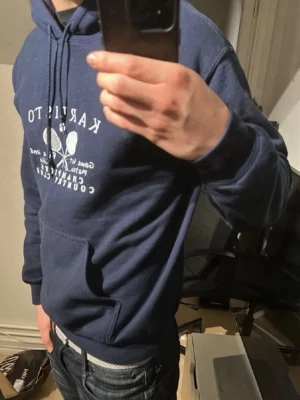 Blå hoodie Karisto Tennis Club - Mörkblå hoodie från Karisto Tennis Club med vit tryckt logga och text på bröstet. Hör av dig vid funderingar!
