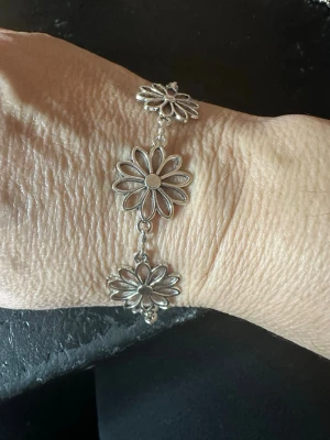 Silverfärgat armband med blommor - Snyggt armband i silverfärg med flera stora, öppna blomformade länkar som ger en cool och unik look. Armbandet har ett magnetlås och är tillverkat i metall. Perfekt för dig som gillar detaljerade smycken med blommotiv.