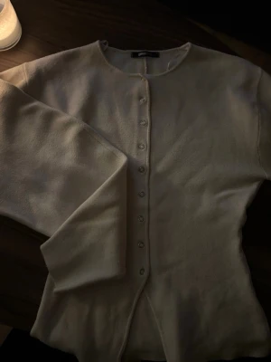 Långärmad från Gina Tricot - Stilren beige kofta från Gina Tricot med rund halsringning och knappar framtill. Använd endast ett fåtal gånger och inga tecken på skavanker.