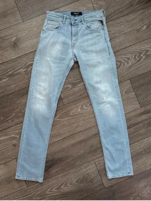 Ljusblå slim fit jeans från Replay - Snygga ljusblå slim fit jeans från Replay med klassisk femficksmodell och diskreta slitningar framtill. Jeansen har en patch med Replay-logga på bakfickan och är tillverkade i mjukt denimtyg. Perfekta för en avslappnad och trendig look. 29/32