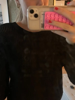 Svart stickad tröja med volangärm - Säljer en svart stickad tröja med rund hals och fina volangdetaljer vid ärmsluten. Tröjan har ett lätt genombrutet mönster som ger en luftig känsla och är perfekt för lager på lager. Passar dig som gillar en enkel men ändå trendig look.