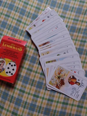 Lenormand spåkortlek med ask - Säljer en Lenormand spåkortlek med original röd ask. Korten har färgglada illustrationer och klassiska symboler, perfekta för tarot och spådom. Text på nederländska och tyska. Asken är dekorerad med spelkortsmotiv och porträtt.