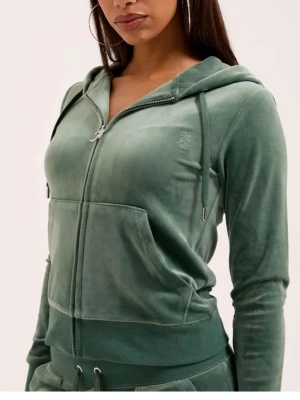 Grön velour hoodie från Juicy Couture - Snygg grön hoodie i mjuk velour från Juicy Couture. Dragkedja framtill, stor ficka och broderad logga på bröstet. Huva med dragsko och ribbade muddar vid ärmslut och midja. Perfekt för en chill och trendig look.