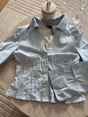 shaped shirt - Snygg ljusblå skjorta med tunna vita ränder, v-ringad och figursydd passform. Skjortan har klassisk krage, långa ärmar och knappar framtill. Perfekt för en stilren look.