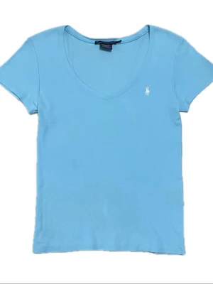 Ljusblå v-ringad t-shirt från Ralph Lauren - Snygg ljusblå t-shirt från Ralph Lauren med v-ringning och korta ärmar. Klassisk liten logga broderad i vitt på bröstet. Perfekt basic-plagg i mjuk bomull som passar till allt.