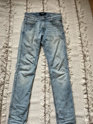 Ljusblå slim fit jeans från Replay - Säljer ett par ljusblå slim fit jeans från Replay med klassisk femficksdesign och snygga slitningar. Jeansen har dragkedjegylf och Replay-logga på linningen. Perfekta för en avslappnad och trendig look.