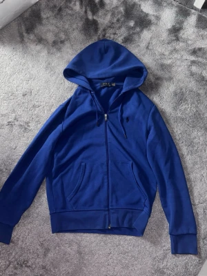 Blå hoodie från Polo Ralph Lauren - Säljer denna snygga Polo Ralph Lauren zip-up pågrund av att den är för liten för mig. Tröjan är väldigt bekväm och är perfekt nu till våren. Pris kan diskuteras!