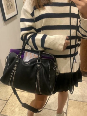 Svart Zadig & Voltaire handväska - Säljer en svart handväska från Zadig & Voltaire i mjukt läder med silverfärgade dragkedjor och nitar. Väskan har både handtag och en justerbar axelrem med logotyp, samt dekorativ metallvinge framtill. Nypriset ligger på ca 6000kr, och den är i, i princip nytt skick, därav pris. Tveka inte att buda eller ställa frågor! 🤗⭐️ (Väskan säljs då den inte kommer till användning längre, tryck ej på köp nu‼️)