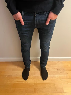 Mörkblå anbass jeans från Replay - Säljer ett par mörkblå skinny jeans från Replay med klassisk femficksdesign och snygga slitningar. Jeansen har en tajt passform och är tillverkade i stretchigt denimtyg för extra komfort. Perfekta för dig som gillar en modern och slimmad stil.