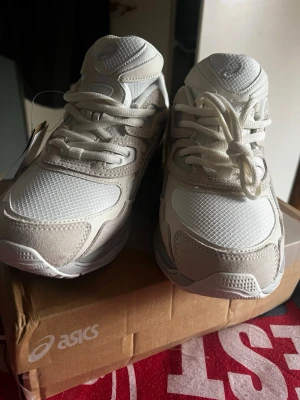 Vita Asics sneakers med mesh och mocka - Snygga vita Asics sneakers med ovandel i mesh och detaljer i mocka. Skorna har en chunky sula och klassisk Asics-logga på sidan. Perfekta för dig som gillar stilrena och sportiga sneakers med modern vibe.