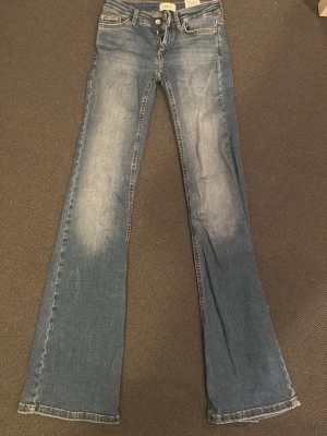 Blå bootcut jeans från ONLY - Säljer ett par ljusblå bootcut jeans från ONLY med klassisk femficksmodell och slitna detaljer på låren. Jeansen har hög midja och utsvängda ben, perfekta för en trendig och avslappnad look. Tillverkade i mjuk denim med snygga kontrastsömmar.