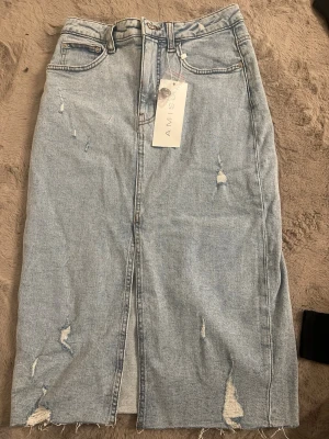 Ljusblå jeanskjol från Amisu - Trendig ljusblå jeanskjol från Amisu med slitna detaljer och rå kant nertill. Kjolen har en rak passform, klassiska fem fickor och en slits framtill för extra edge. Perfekt för dig som gillar en avslappnad och cool stil.