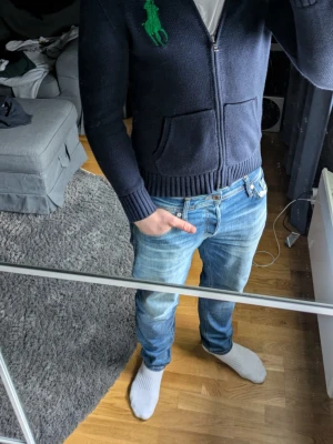 Marinblå stickad ziptröja Polo Ralph Lauren - Mörkblå stickad ziptröja från Polo Ralph Lauren med stor grön logga på bröstet och grön siffra på ärmen. Tröjan har två fickor fram, ribbade muddar och midja samt dragkedja hela vägen. Klassisk och sportig look i mjukt stickat material. Riktigt snygg tröja, går att diskutera pris, hör av er vid minsta fråga