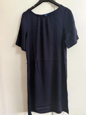 Mörkblå enkel kortklänning från Gant - En stilren mörkblå kortklänning med rund halsringning och korta ärmar. Klänningen har en rak passform och är tillverkad i ett mjukt, lätt material som ger ett snyggt fall. Perfekt för dig som gillar minimalistisk och clean stil.