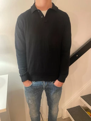 Selected Homme tröja  - Klassisk svart långärmad pikétröja med krage och knappar vid halsen. Tröjan har ribbade muddar vid ärmslut och nederkant för en snygg passform. Väldigt stilren och snygg. Skick är 8/10, lite använd. Nypris 600 kr