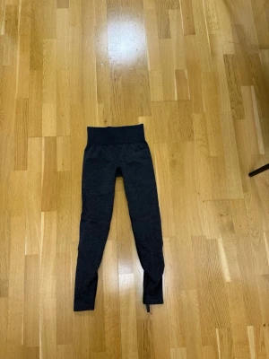 Mörkgrå sömlösa leggings - Snygga mörkgrå leggings med hög midja och sömlös design från ICIW. Materialet är stretchigt och mjukt, perfekt för träning eller chill. Diskreta svarta detaljer på baksidan av benen ger en sportig look. Inget synligt märke.