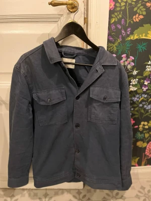 Mörkblå overshirt med fickor - Snygg mörkblå overshirt i bomull med klassisk krage och två bröstfickor med knappar. Rak passform och knäppning framtill. Perfekt lager-på-lager-plagg för en avslappnad stil.