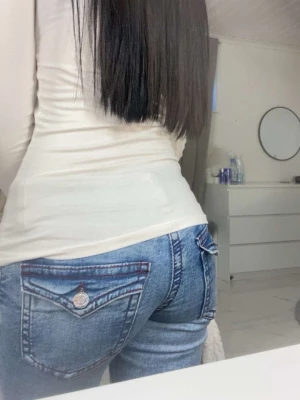 Gina tricot Ljusblå slitna bootcut jeans  - Säljer ett par ljusblå bootcut jeans med slitningar och snygga detaljer på bakfickorna. Jeansen har låg midja och dekorativ knapp på fickan. Perfekta för en avslappnad och trendig look. Materialet är klassisk denim.