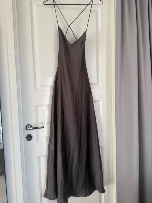 Klänning Zara - Säljer en elegant mörkbrun långklänning med tunna axelband och öppen rygg. Klänningen har en slät, glansig yta och prislapp sitter kvar. Storlek XS men passar även S