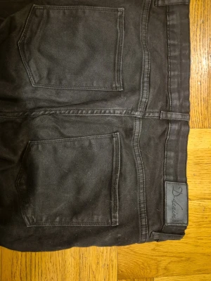 Strechiga Svarta stuprörs jeans - Svarta jeans från D-denim by gekås med klassisk femficksmodell och raka ben. Jeansen har silverfärgade nitar och bälteshällor. Materialet är strechig denim. Svarta och lite ljusare i sömmar