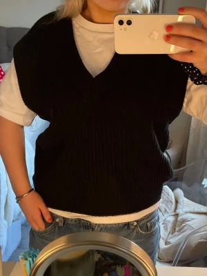Svart stickad väst med v-ringning - Säljer en svart stickad väst med djup v-ringning. Perfekt att bära över en t-shirt eller skjorta för en trendig lager-på-lager-look. Västen har en loose passform och är enkel att styla till både jeans och kjol.