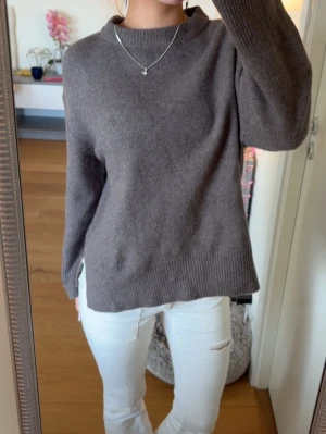 Brun stickad tröja med slits - Mysig brun stickad tröja med rund hals och långa ärmar. Tröjan har ribbade muddar och en liten slits i sidan nedtill för extra detalj.