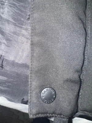 Svart dunväst från Canada Goose - Stilren svart dunväst från Canada Goose med klassisk quiltad design och hög krage. Västen har tryckknappar med varumärkeslogga och är perfekt för lager-på-lager-stil under kyliga dagar.