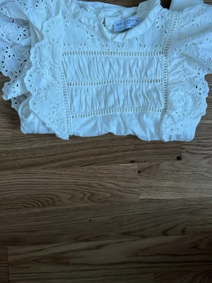 Vit blus med broderi från Holly & Whyte (LINDEX) - Supersöt vit blus från Holly & Whyte by Lindex med broderade detaljer och volang vid axlarna. Blusen har fina hålbroderier och rynkade partier framtill och lite där bak. Passar bra på midsommar eller en skolavslutning💞💞Perfekt för dig som gillar en feminin och somrig stil. (Använd en gång och pris kan alltid diskuteras)