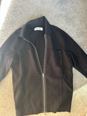 Svart ziptröja från Samsoe Samsoe  - Svart tröja med dragkedja från Samsoe Samsoe. Tröjan har en klassisk krage, en bröstficka och är tillverkad i ett mjukt material. Enkel och stilren design som passar till många olika looks. Perfekt till våren som sommaren. Hör av er vid frågor eller funderingar. 