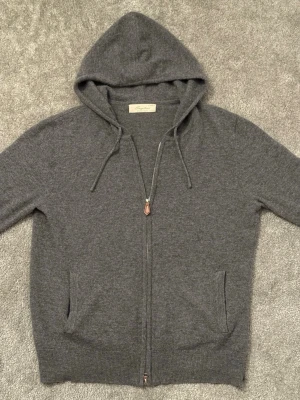 Mörkgrå hoodie från Sayless - Mörkgrå hoodie från Sayless med dragkedja framtill, två fickor och justerbar huva med snören. Tillverkad i mjukt material som känns skönt mot huden. Perfekt för en avslappnad och stilren look. Nästan helt ny, knappt använd. 100% Cahsmere