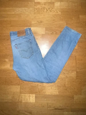 Levi's ljusblå raka jeans - Säljer ett par klassiska ljusblå jeans från Levi's med rak passform och hög midja. Jeansen har fem fickor, Levi's ikoniska röda etikett på bakfickan och ett brunt läderpatch bak i midjan. Perfekta för en avslappnad och tidlös stil.
