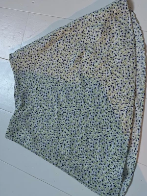 Blommig kortkjol i ljusa färger - Söt kortkjol med småblommigt mönster i blått, grönt och vitt. Kjolen har en lätt A-linjeform och är fodrad för extra komfort. Perfekt för vår och sommar, enkel att matcha med olika toppar.