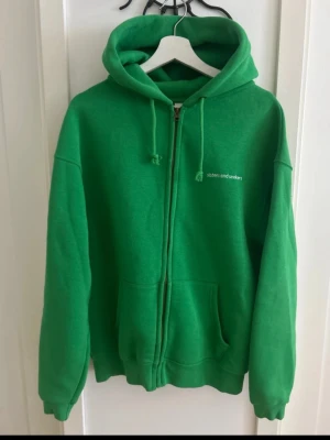 Grön zip hoodie Sisters and Seekers - Grön hoodie med dragkedja från Sisters and Seekers. Klassisk modell med huva och dragsko, samt fickor framtill. Liten vit logga på bröstet. Perfekt oversized look och mjukt material, troligen bomullsblandning.