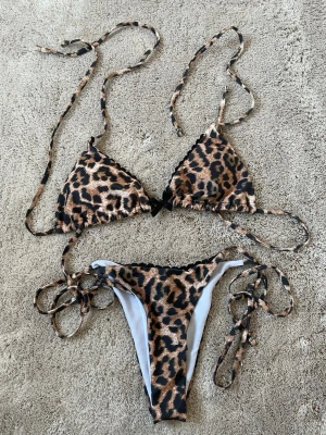 Leopardmönstrad bikini med knyt - Trendig bikini med leopardmönster och knyt i sidorna samt bakom nacken och ryggen. Klassisk trekantsmodell upptill och matchande trosa. Perfekt för dig som vill sticka ut på stranden.