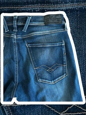  Replay anbass - Snygga blå jeans från Replay med raka ben och klassisk femficksmodell. Jeansen har dekorativa sömmar på bakfickorna och en mörk tvätt med lätt slitning. Tillverkade i denim med skinnpatch bak i midjan. Perfekta för en avslappnad och trendig look.