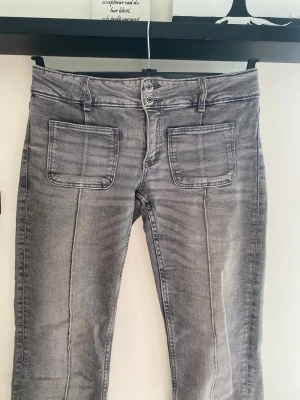Grå jeans med raka ben  - Säljer ett par superfina grå jeans med raka ben och stora fyrkantiga fickor framtill. Jeansen har dubbla knappar i midjan och markerade sömmar längs benen. Materialet är klassisk denim med en tvättad look. 