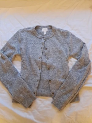 grå kofta från H&M - mysig grå kofta från H&M med rund halsringning och brun-beiga knappar💕max använd 3 gånger!