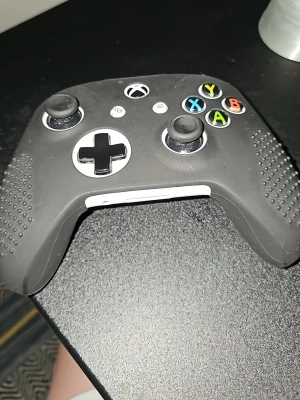 Svart Xbox-handkontroll med silikonfodral - Säljer en svart Xbox-handkontroll med greppvänligt silikonfodral. Handkontrollen har klassiska färgade knappar (A, B, X, Y), två styrspakar och styrkors i silver. Perfekt för gaming och passar till Xbox-konsoler.