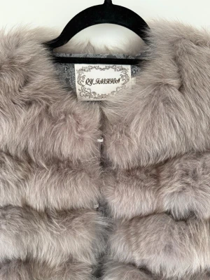 Ljusgrå pälsjacka i äkta räv (fjällräv) - En fantastiskt fin och lyxig pälsjacka i äkta räv(fjällräv) i en vacker ljusgrå nyans. Det är en praktisk transformer-modell som kan användas på flera sätt eftersom både ärmarna och den nedersta delen är avtagbara med dolda dragkedjor. Du kan enkelt förvandla den till en kortare pälsjacka eller en snygg palsvast beroende på väder och stil. Jackan är i absolut nyskick och har endast använts vid tre tillfällen. en är mycket fluffig, varm och val omhändertagen utan några som helst tecken på slitage