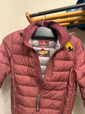 Vinröd dunjacka från Parajumpers - Snygg vinröd dunjacka från Parajumpers med quiltad design och gul detalj vid kragen. Jackan har två dragkedjeförsedda fickor framtill och en hög krage. Insidan är ljusgrå och materialet är lätt och smidigt, perfekt för kyliga dagar och även vår dagar!    Jackan är köpt på kidsbrandstore och säljs nu pågrund av att jag har växt ut den för ett tag sen! Jackan är köpt för ca 4000kr 