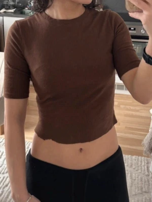 Brun ribbad croppad topp - Snygg brun croppad topp med ribbad struktur och korta ärmar. Perfekt till höga jeans eller kjol för en trendig look. Materialet känns mjukt och stretchigt, vilket gör den bekväm att bära hela dagen.