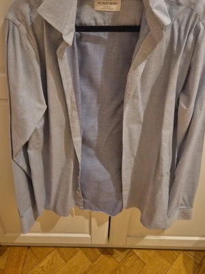 Blå slim fit skjorta The Shirt Factory - Snygg blå skjorta från The Shirt Factory i slim fit-modell. Skjortan har diskret rutigt mönster, klassisk krage och knappar framtill. Tillverkad i lättskött bomull som är lättstruken. Perfekt för en clean och stilren look.