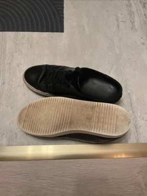 Svarta sneakers från Axel Arigato - Snygga svarta sneakers från Axel Arigato i läder med vit sula och diskret logga på sidan. Klassisk låg modell med svarta skosnören och stilren design som passar till det mesta.